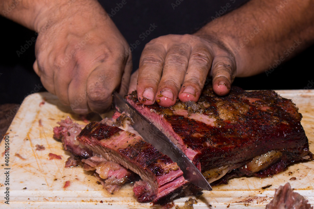 Tasty smoked beef rib being sliced ​​with a knife. Slices with light pink. Rustic food made on the grill and smoked at Pit Smoker. Cutting meat. Close-up photography.