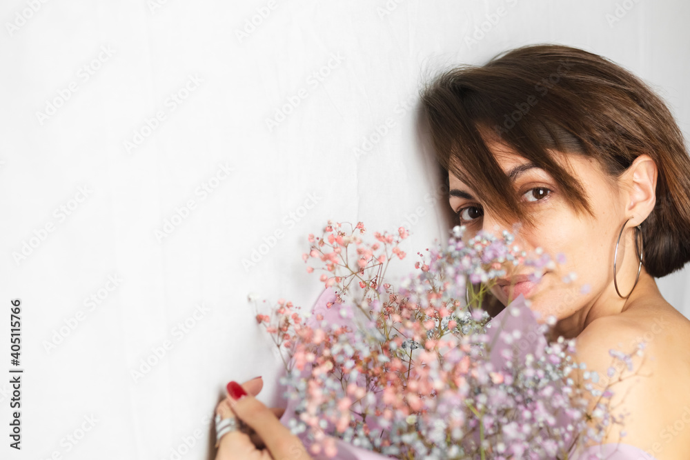 Gentle portrait of a young woman on a white rag background topless holding a bouquet of dry multi-colored flowers and smiling cute, anticipation of spring