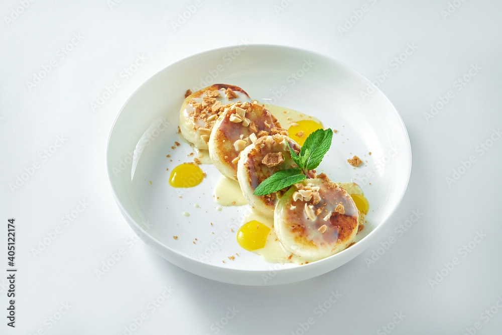 Delicious Ukrainian breakfast - cheesecakes with nuts, mango and white sweet sauce in a white plate. on white background. Syrniki