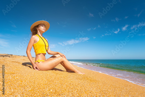 Wallpaper Mural Attractive young woman in a yellow swimsuit and a straw hat. Sits on a golden beach and azure sea with eyes closed from pleasure Torontodigital.ca