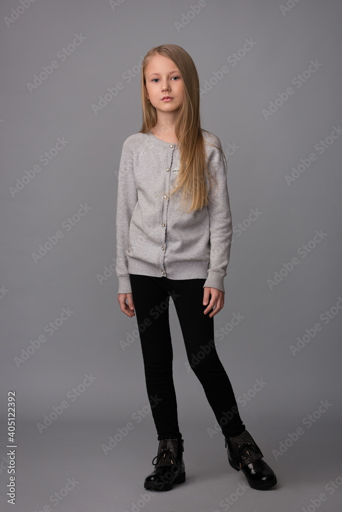 girl child in a gray sweater and black pants on a gray background girl child in a gray sweater and black pants on a gray background