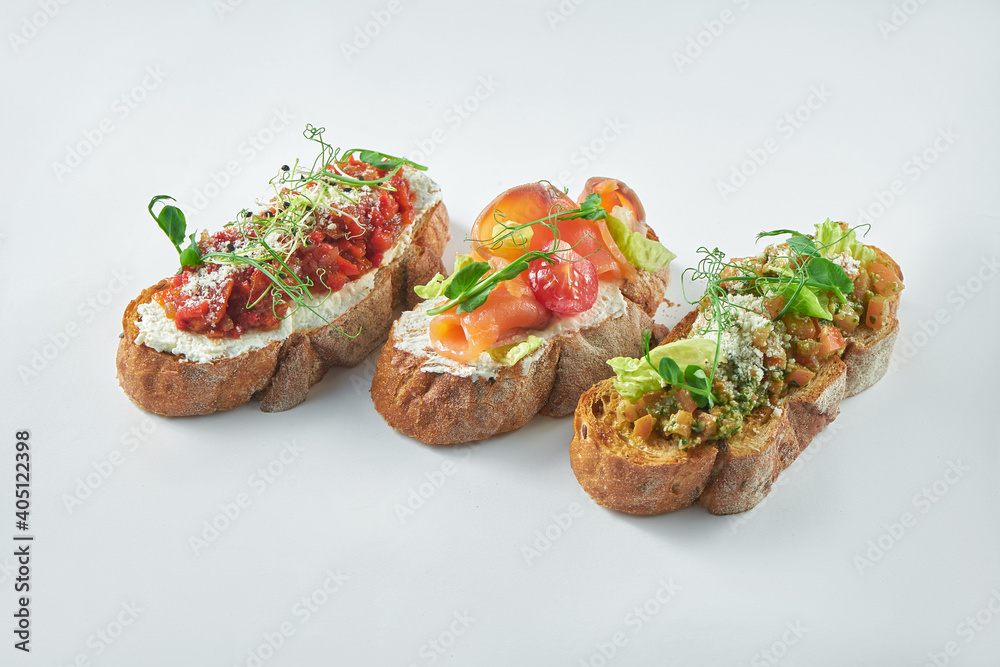Italian appetizer - three bruschetta with tomatoes, salmon and baked peppers on a white background
