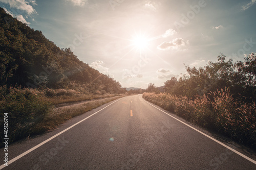 Empty asphalt road through the green field and clouds on blue sky.