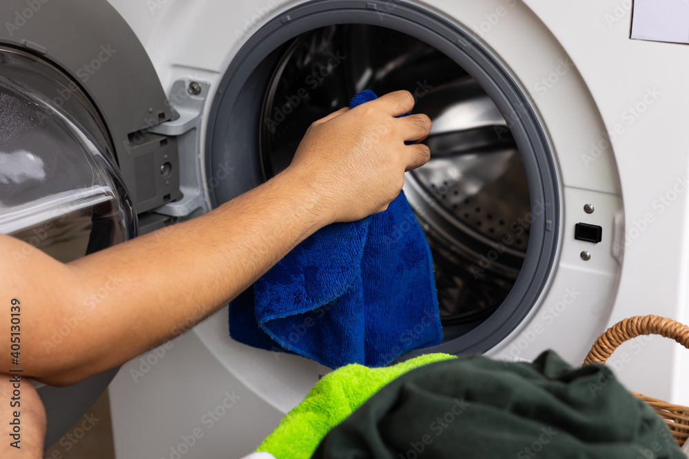 Man's hand opening the front of the washing machine And is about to put the dirty laundry into the wash Man's hand opening the front of the washing machine And is about to put the dirty laundry into the wash