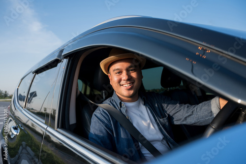 A young Asian man drives a car on a clear day. With beautiful blue sky. He driving to travel by car.