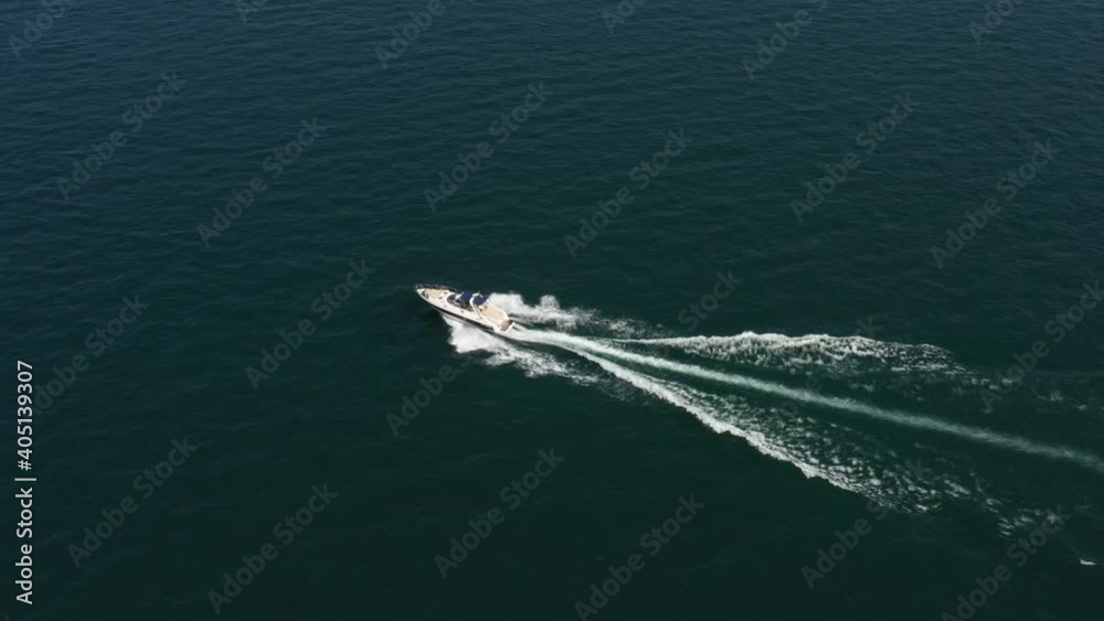 Aerial view of luxury white boat fast movement on water. Drone view of a boat the blue waters. White large yacht at high speed in the sun. Aerial view. People on the boat. Aerial view of luxury white boat fast movement on water. Drone view of a boat the blue waters. White large yacht at high speed in the sun. Aerial view. People on the boat.