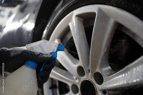 Auto detailing worker applies chemistry to wheels. Professional car wheel wash photo