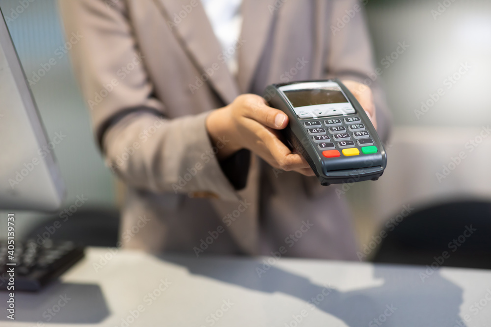 Female receptionist employee holding card reader machine on hand at checkout counter. Female receptionist employee holding card reader machine on hand at checkout counter.