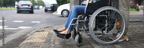 Close-up of man accompany female in wheelchair. Person taking care of lover. Carefully crossing street. Lady in jeans and blue shirt. Walk in city. Disabled people concept