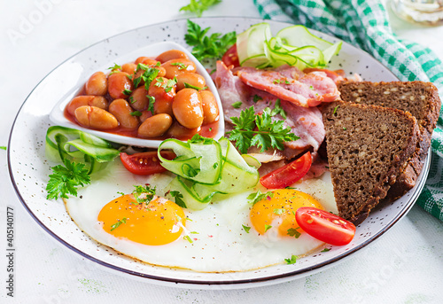 English breakfast - fried egg, beans, bacon, tomatoes and bread.