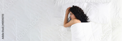 Top view of young woman peacefully sleeping in comfy bed at home. Good night sleep. Female laying under nice bedding. Shape on body. Rest and sweet dreams concept
