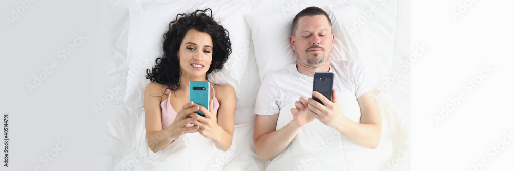 Top view of couple laying in bed and using smartphones. Woman and man holding mobile phones and surfing on internet. Social media in life. Good morning and wake up concept Top view of couple laying in bed and using smartphones. Woman and man holding mobile phones and surfing on internet. Social media in life. Good morning and wake up concept