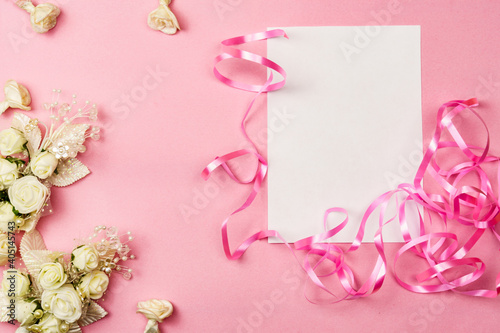 Beautiful valentine's day concept with copy space. White sheet of paper, artificial flowers on a pink background.