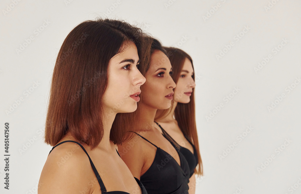 Side view. Three young women in lingerie together indoors. White background Side view. Three young women in lingerie together indoors. White background