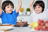 Heroes of the occasion. Excited little hispanic twins looking happy after blowing candles on a birthday cake. Children celebrating birthday together with parents at home