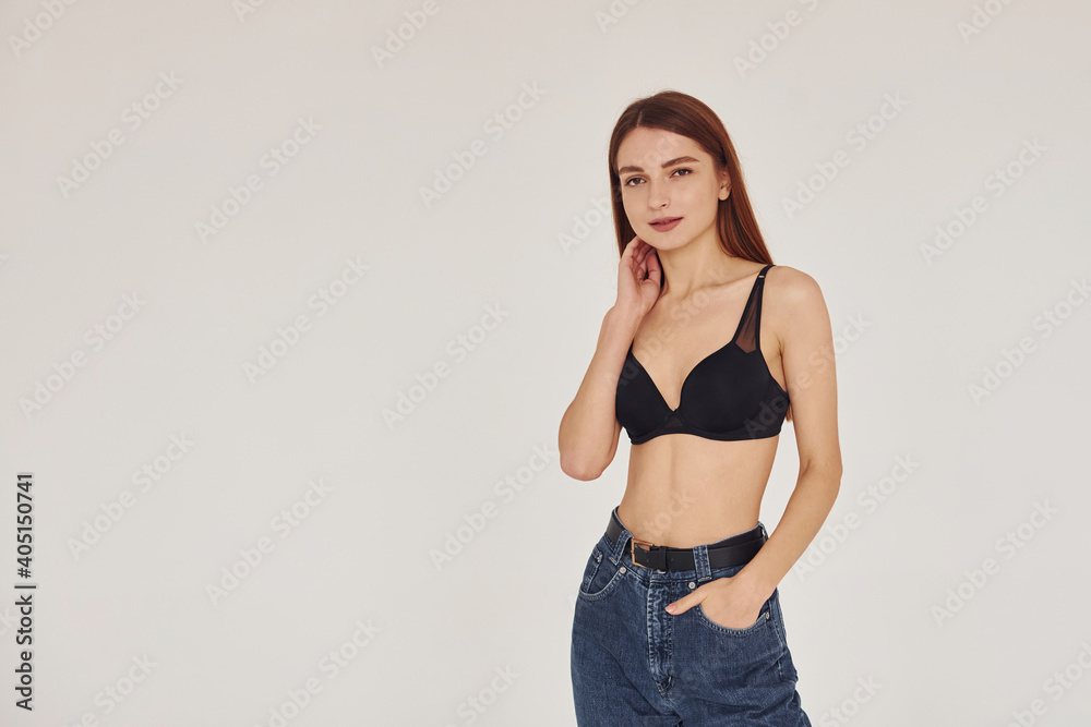 Young woman in jeans and bra indoors. White background Young woman in jeans and bra indoors. White background