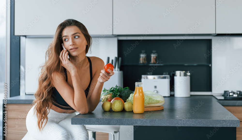 Talks by the phone. Young european woman is indoors at kitchen indoors with healthy food Talks by the phone. Young european woman is indoors at kitchen indoors with healthy food