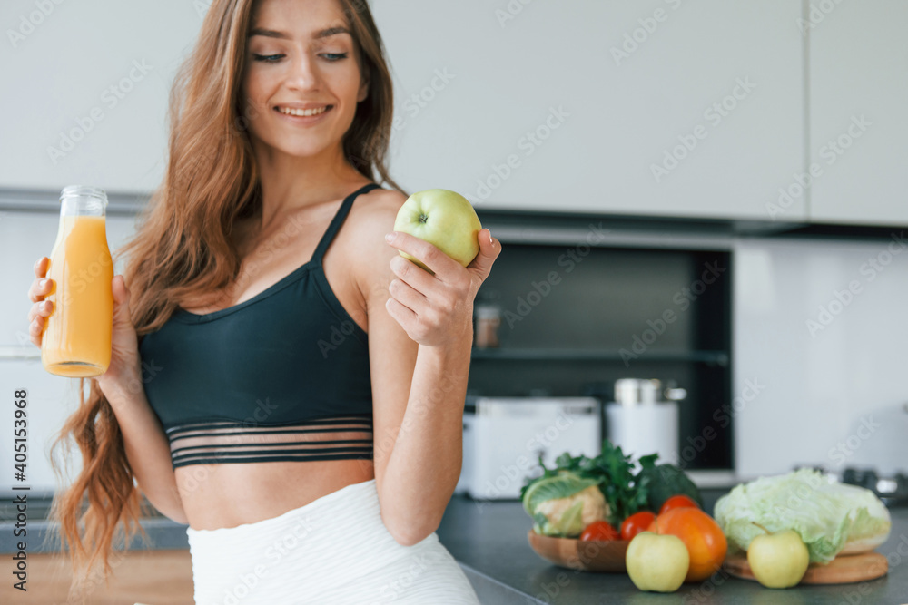 Holds apple in hand. Young european woman is indoors at kitchen indoors with healthy food Holds apple in hand. Young european woman is indoors at kitchen indoors with healthy food
