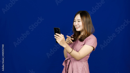 Portrait of Asian woman pointing her smart phone isolated blue background