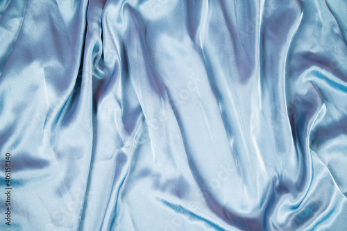 Light blue satin fabric background. Flowing wavy silk fabric background top view