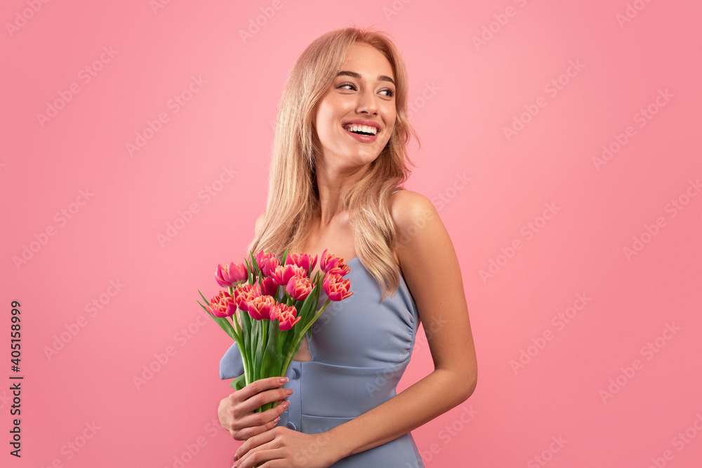 Woman's Day. Attractive young lady with bunch of fresh tulips celebrating spring holiday on pink studio background