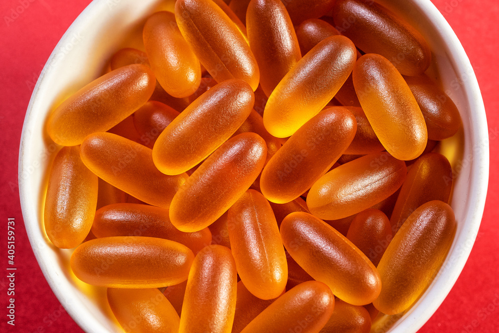 a bowl filled with yellow gelatin capsules on a red background a bowl filled with yellow gelatin capsules on a red background