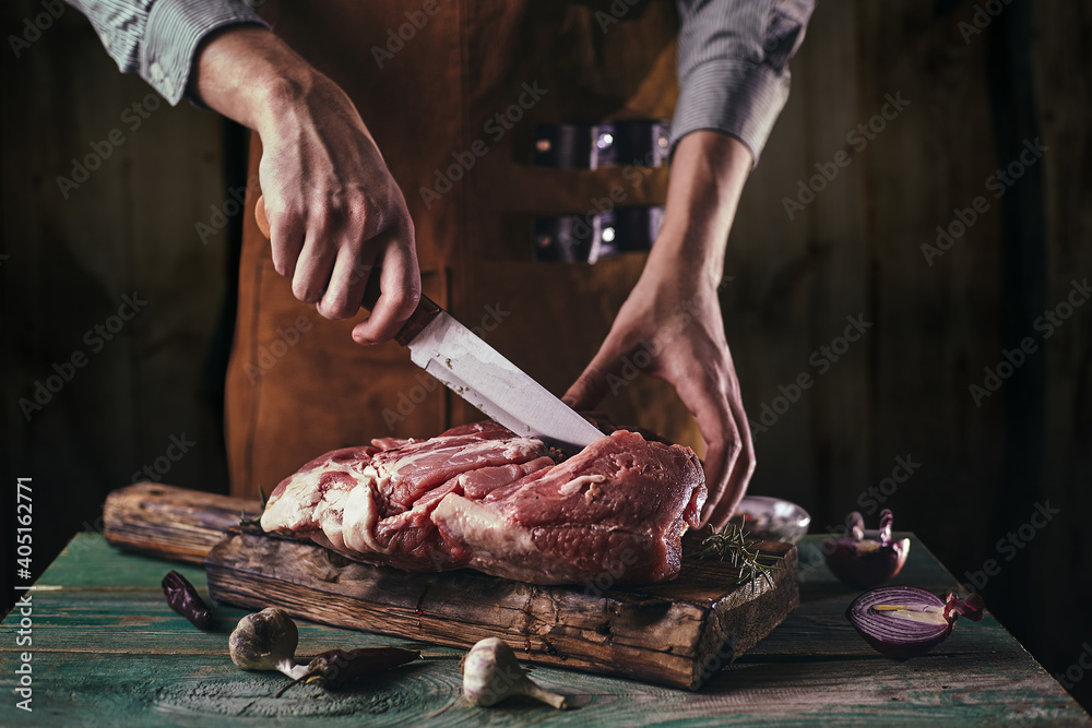 A butcher in a leather apron cuts a large piece of meat on a wooden board..