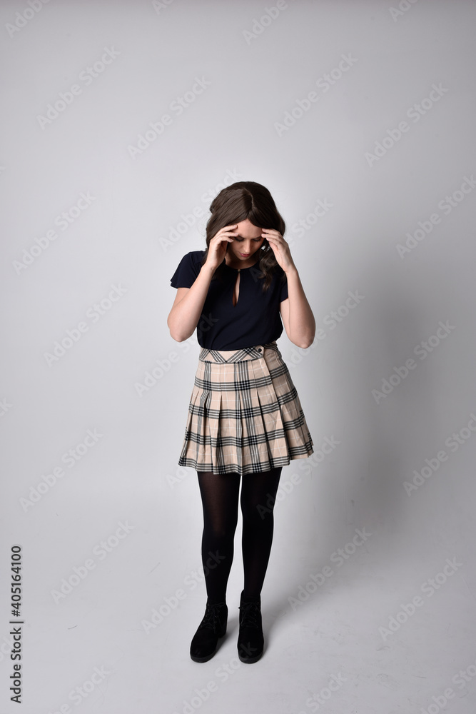 Full length portrait of pretty brunette woman wearing tartan skirt and blouse. Standing pose on the ground, against a studio background. Full length portrait of pretty brunette woman wearing tartan skirt and blouse. Standing pose on the ground, against a studio background.
