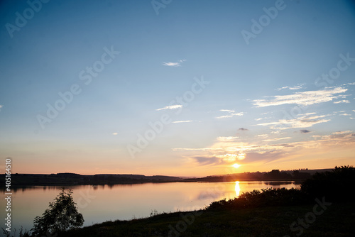 Beautiful lake view during sunset with blue and yellow sky reflection in water. Rural scene. Ecological protection and eco tourism concept. Natural landscape. Isolation in countryside. © Natalia