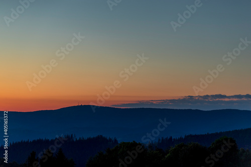 Sun setting over a horizon of orange hills with a coniferous tree on the left and clouds moving in the background over the Beskydy countryside. © Lukas