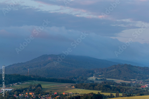 Landscape full of hills and mountains with clouds and blue sky with sun during colorful sunset Beskydy region.