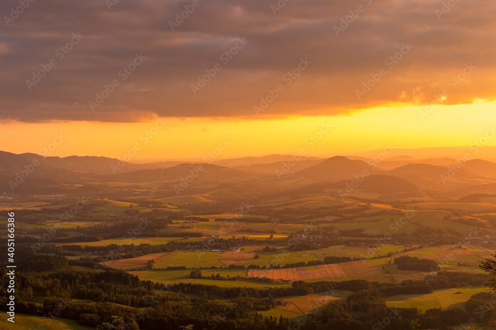A view of a landscape full of mountains during a golden sunset with the sun on the horizon and a view of the sun from the top of Mount Ondrejnik.