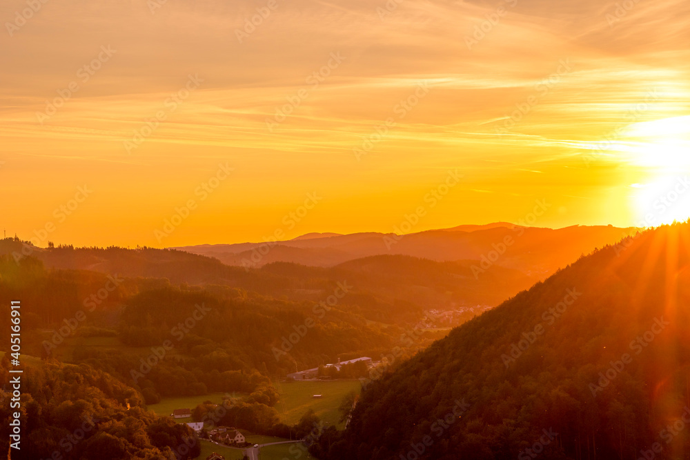 Setting sun in a valley landscape flooded with orange gold color moving beyond the horizon overlooking the mountains and surrounding hills.