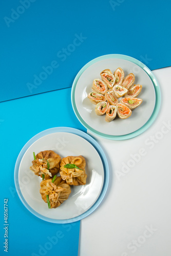 Top view of Two types of Russian traditional crepes. Blini with meat and salmon fish. Christmas holiday dishes. New year serving. Thin Russian pancakes served on blue colorful abstract background. 