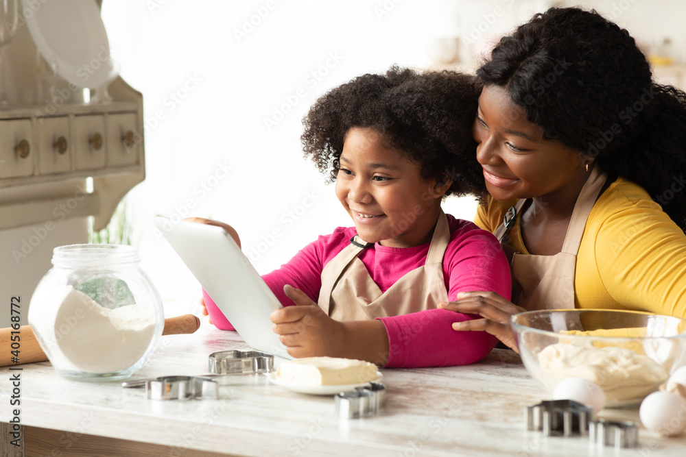 Cute Black Little Girl And Mom Checking Cookies Recipe On Digital Tablet Cute Black Little Girl And Mom Checking Cookies Recipe On Digital Tablet
