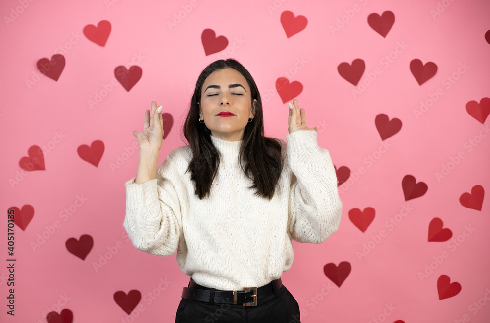 Young beautiful woman over pink background with harts relax and smiling with eyes closed doing meditation gesture with fingers Young beautiful woman over pink background with harts relax and smiling with eyes closed doing meditation gesture with fingers