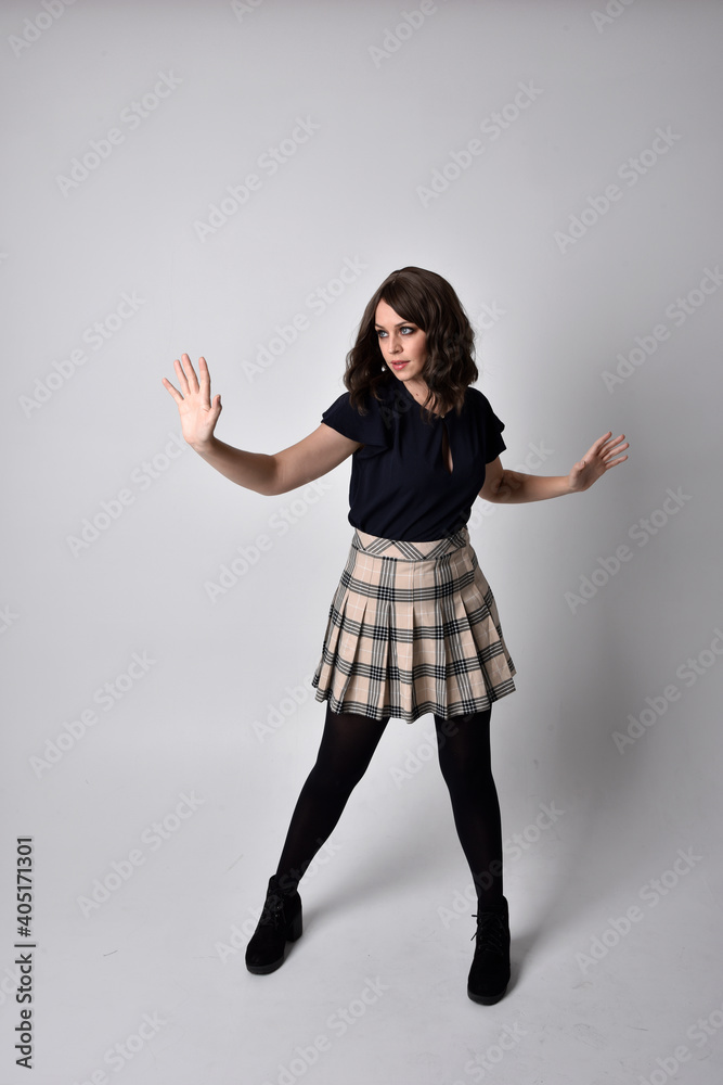 Full length portrait of pretty brunette woman wearing tartan skirt and blouse. Standing pose on the ground, against a studio background. Full length portrait of pretty brunette woman wearing tartan skirt and blouse. Standing pose on the ground, against a studio background.