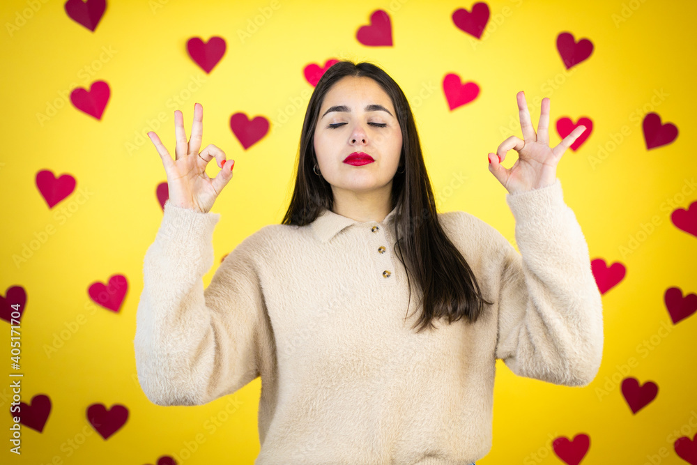 Young caucasian woman over yellow background with red hearts relax and smiling with eyes closed doing meditation gesture with fingers Young caucasian woman over yellow background with red hearts relax and smiling with eyes closed doing meditation gesture with fingers