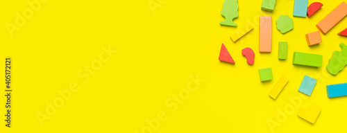 Multi-colored children's constructor made of natural wood on bright yellow background flat lay top view. Colored children's bricks for construction. Building blocks background. Developing toys, game