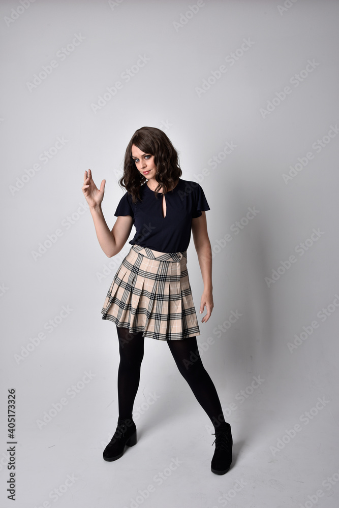 Full length portrait of pretty brunette woman wearing tartan skirt and blouse. Standing pose on the ground, against a studio background. Full length portrait of pretty brunette woman wearing tartan skirt and blouse. Standing pose on the ground, against a studio background.