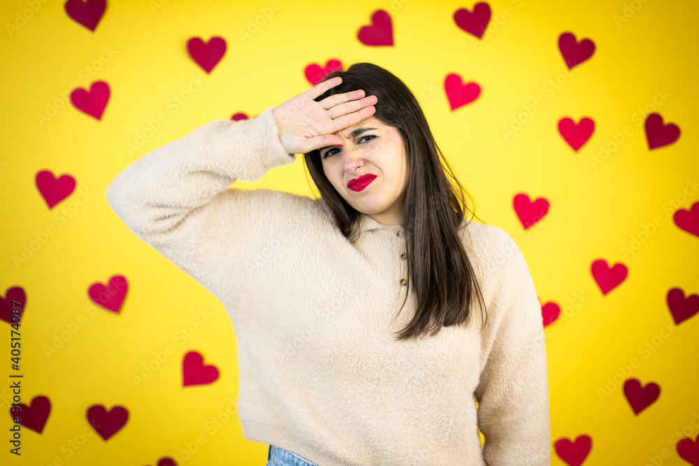 Young caucasian woman over yellow background with red hearts Touching forehead for illness and fever, flu and cold, virus sick Young caucasian woman over yellow background with red hearts Touching forehead for illness and fever, flu and cold, virus sick