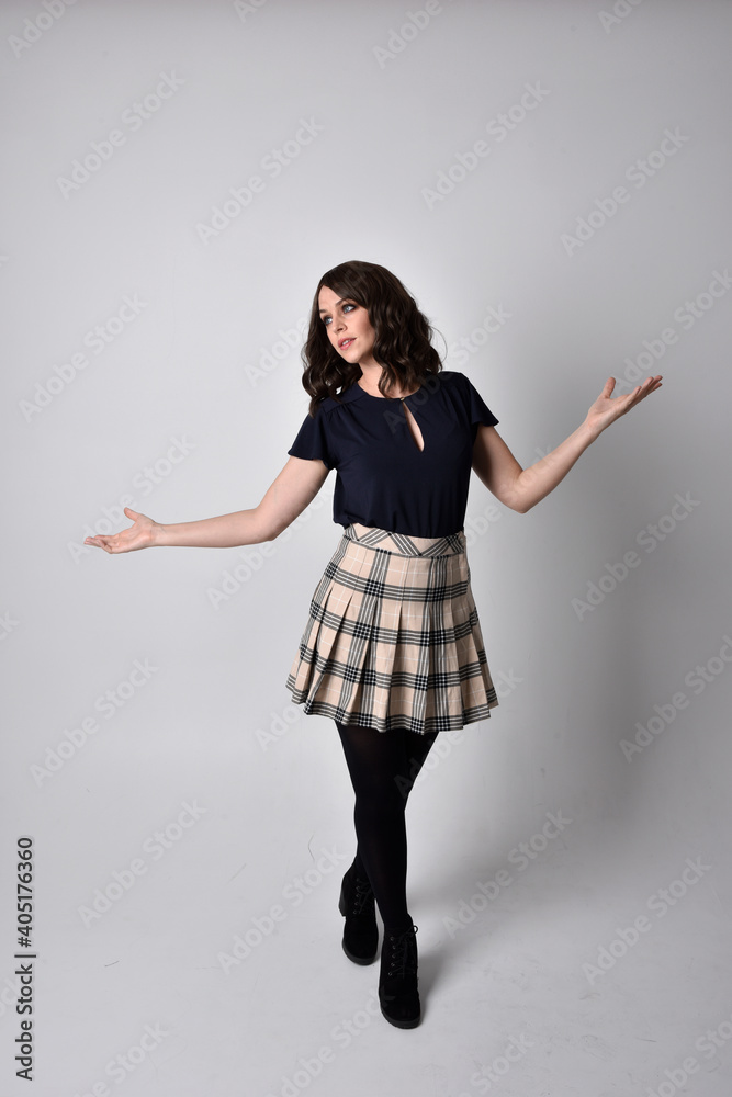 Full length portrait of pretty brunette woman wearing tartan skirt and blouse. Standing pose on the ground, against a studio background. Full length portrait of pretty brunette woman wearing tartan skirt and blouse. Standing pose on the ground, against a studio background.