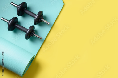 Sport black dumbbells on turquoise yoga mat on yellow background. Copy space. Flat lay. View from above.