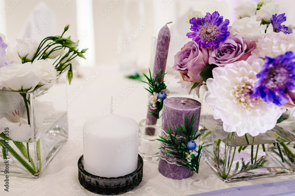 Festive table decorated with composition of violet, purple, pink flowers and greenery, candles in the banquet hall. Table newlyweds in the banquet area on wedding party.