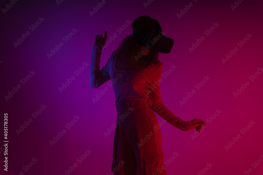 Young woman wear virtual reality VR goggles in neon light background.