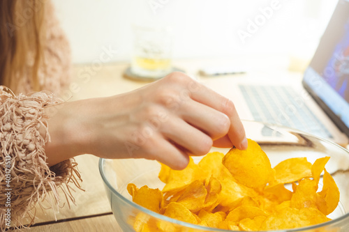 Young woman working at laptop and eating chips