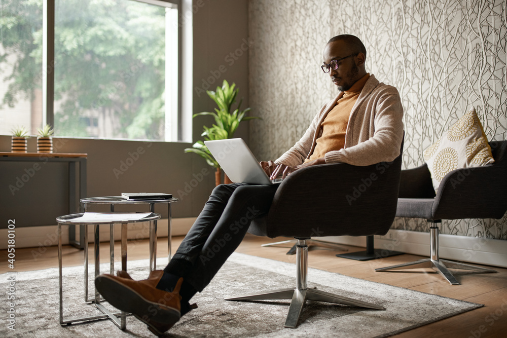 Black african businessman sitting relaxing and typing on laptop