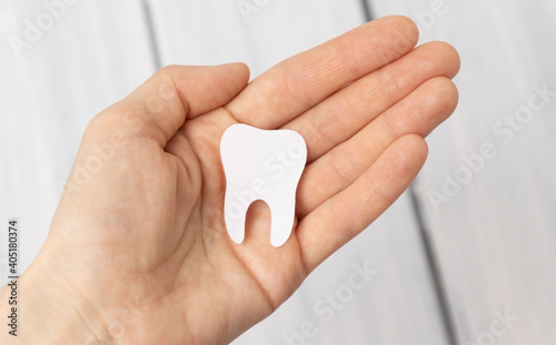 Tooth figurine in hand on wooden background. Means to care for the oral cavity.