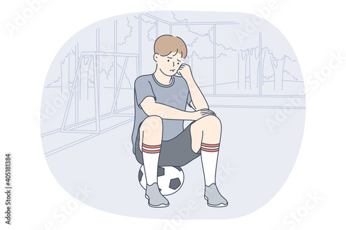 Professional football player, soccer ball, sport concept. Young unhappy boy football player sitting on soccer ball and feeling sad after failure during workout or game. Sport, athletics, team sport 