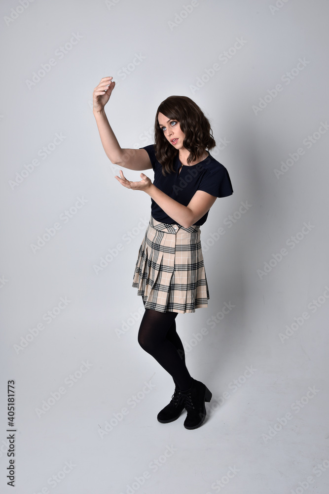 Full length portrait of pretty brunette woman wearing tartan skirt and blouse. Standing pose on the ground, against a studio background. Full length portrait of pretty brunette woman wearing tartan skirt and blouse. Standing pose on the ground, against a studio background.